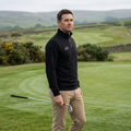 Golfer wearing black Golf quarter-zip holding an iron by the putting green, AI-generated mockup